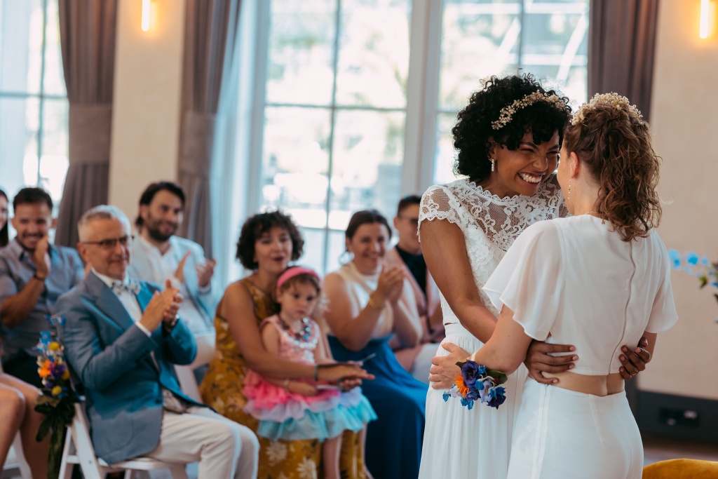 Two women after having said "I do", family is seen cheering in the background